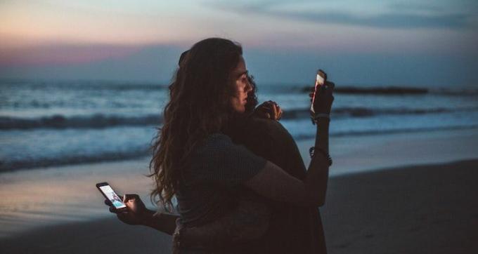 Par se grli i gleda u svoje telefone na plaži