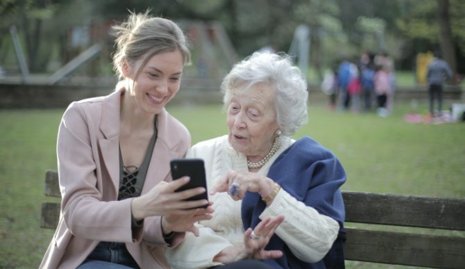 Mlada i starica koja gleda u telefon na klupi