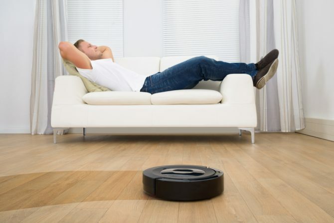 Čovjek opuštajući se na kauču s robotskim usisavačem na podu od tvrdog drva