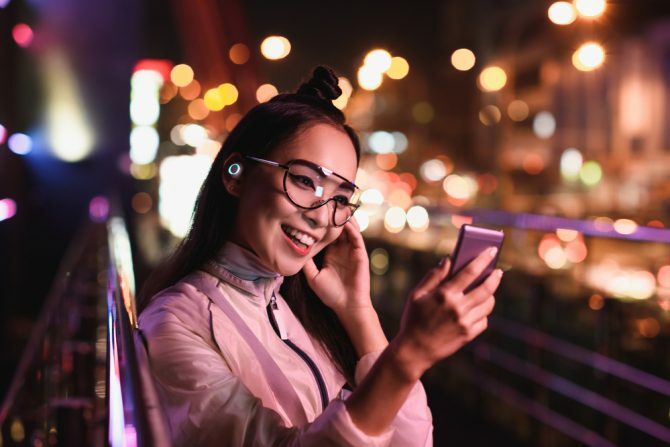 sretna azijska djevojka koja ima video chat pomoću pametnih telefona i u slušalicama